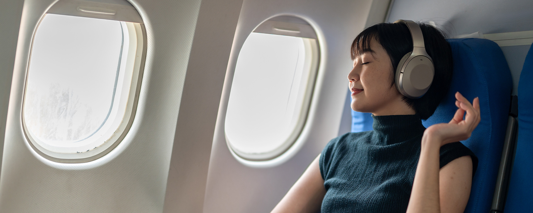 A woman light to music on an airplane while facing the window