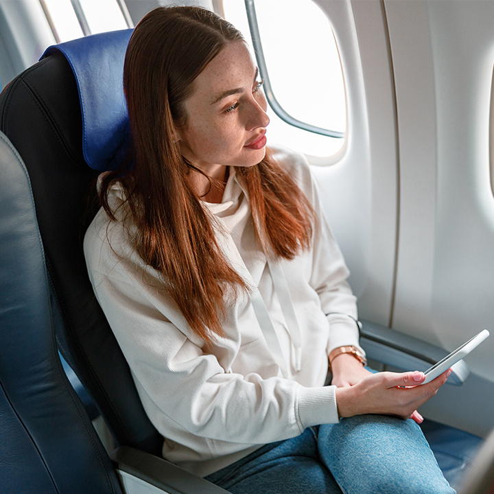 Passenger sitting in an aircraft while holding her phone and looking out the window