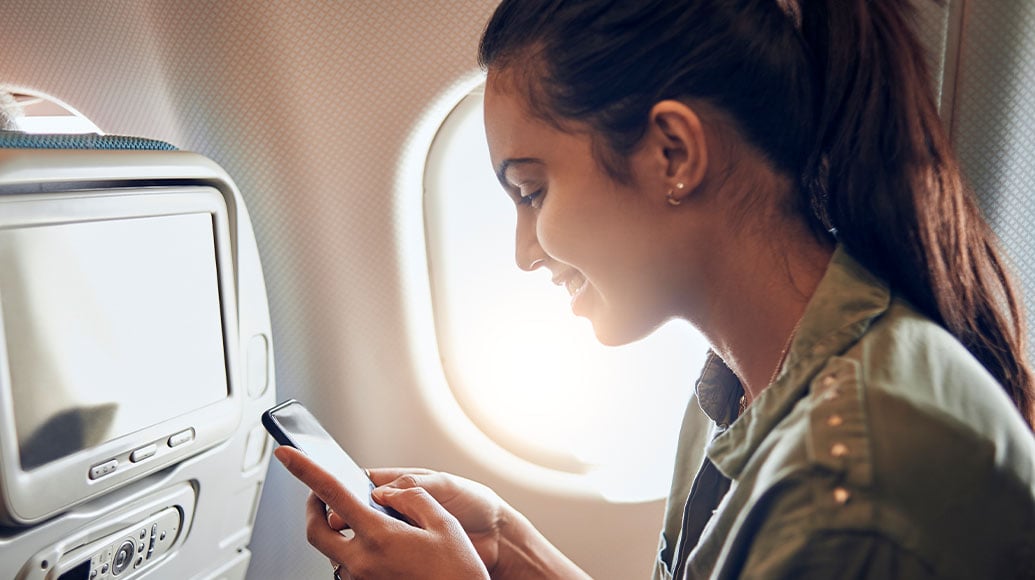 Woman smiling while looking at her smartphone in an airplane seat