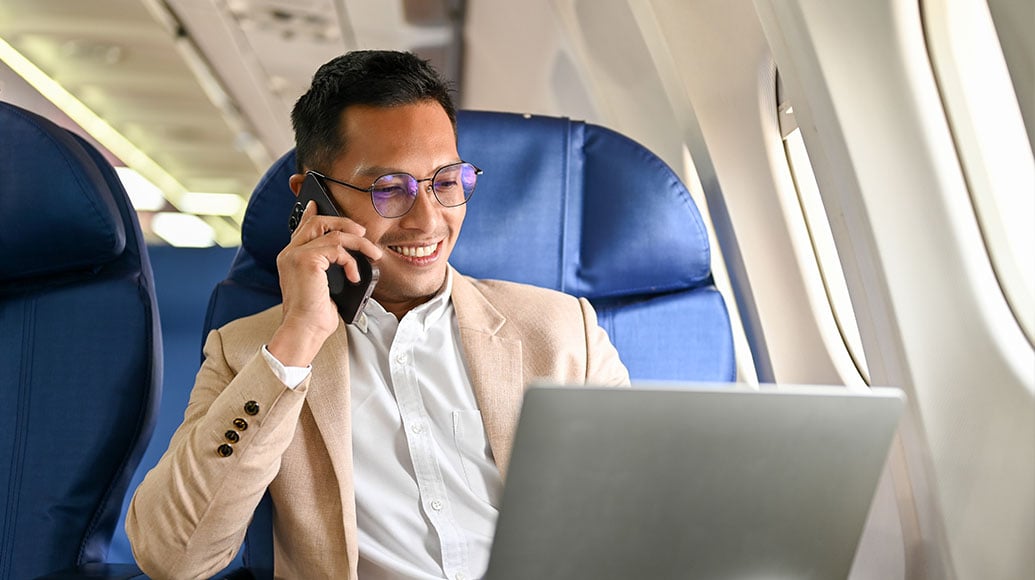 Man on an airplane using a laptop and holding a coffee cup