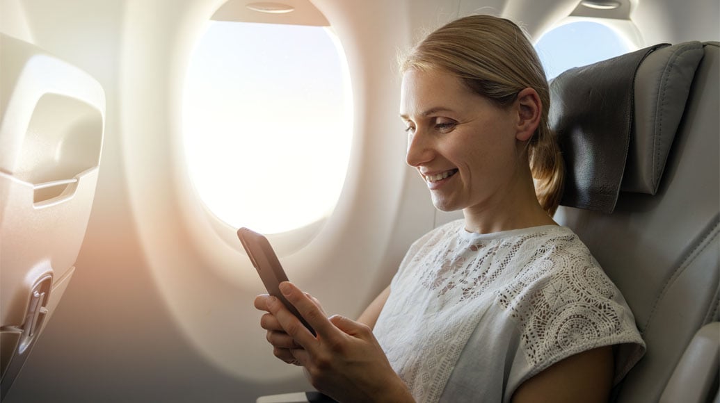 Woman smiling at cell phone next to airplane window