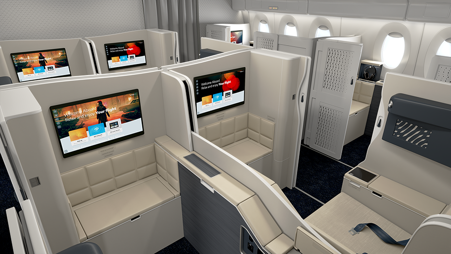 Business class seating in an aircraft with private suites, large screens, beige seats, and dark blue carpet